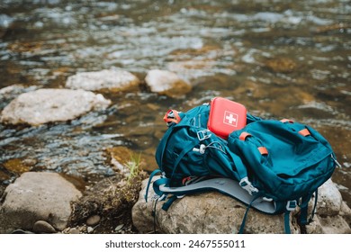 A hiking backpack with a first aid kit sits on a rock by a river. Essential gear for outdoor adventures, highlighting safety and preparedness in nature. Explore the wilderness with peace of mind - Powered by Shutterstock