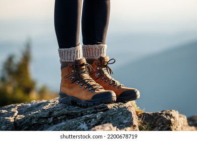 Hiking boot. Female legs with leather ankle shoes and knitted wool socks on mountain peak during trekking outdoors