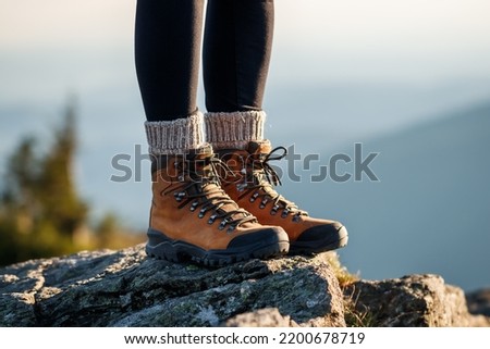 Hiking boot. Female legs with leather ankle shoes and knitted wool socks on mountain peak during trekking outdoors