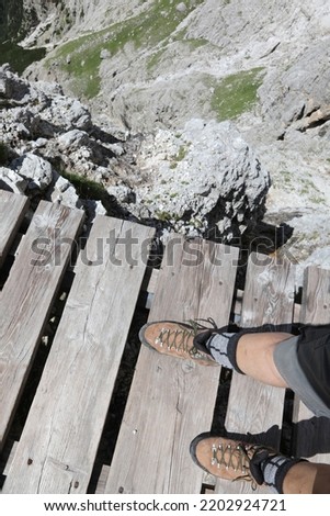 hiking boots of hiker walking on a suspended wooden bridge over the dolomites high mountain precipice of the european alps