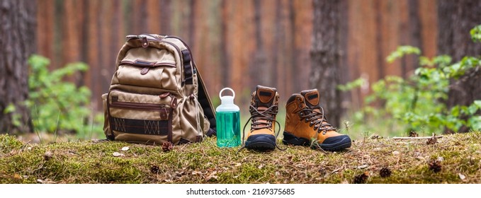 Hiking and camping equipment in forest. Backpack, water bottle and leather ankle boots. Panoramic view with copy space - Powered by Shutterstock
