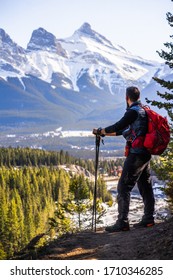 Hiking In Canadian Rockies. Adventurous Man Overlooking Beautiful Mountain Landscape And The Three Sisters Peaks In Canmore, Alberta, Canada 