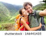 Hiking couple - Active young couple in love. Couple taking self-portrait picture on hike. Man and woman hiker trekking on Waihee ridge trail, Maui, USA. Happy romantic interracial couple.