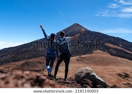 Hiking couple with backpacks holding hand on summit Pico Viejo with scenic view on the peak of volcano Pico del Teide, Tenerife, Canary Islands, Spain, Europe. Volcanic barren solidified lava terrain