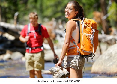 Hiking Friends Having Fun Crossing River In Forest. Young Happy Adults Barefoot Walking In Water With Wet Feet On An Adventure Trip Hike In Nature.