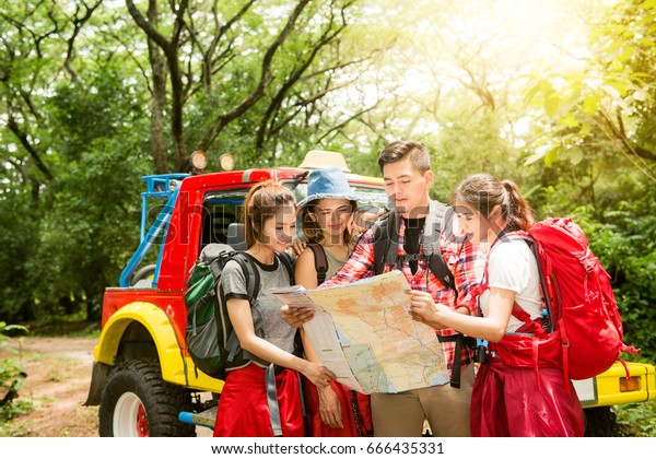 Hiking - hikers looking at\
map. Couple or friends navigating together smiling happy during\
camping travel hike outdoors in forest. Young mixed race Asian\
woman and man