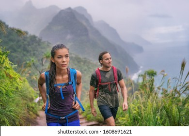 Hiking hikers woman and man trekking on trail trek with backpacks living healthy active lifestyle. Hiker girl walking on hike in mountain nature landscape wet scenery, Na Pali Coast, Kauai, Hawaii. - Powered by Shutterstock