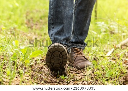Hiking leather brown boots close-up. Man tourist in jeans steps on green grass in nature