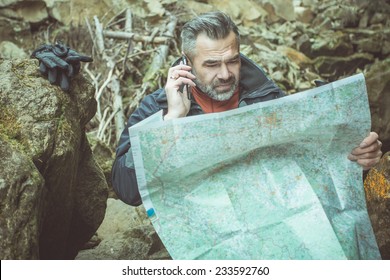 Hiking man in autumn or winter nature holding map outdoors over dark stone mountains in the evening. toned image - Powered by Shutterstock