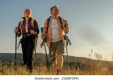 Hiking middle age couple follow trail along grassy mountain ridge