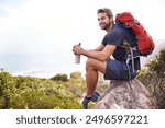 Hiking, mountain and man rest on a rock thinking after exercise, workout and fitness in nature for wellness. Travel, vacation and male person or athlete smile at a view after training and trekking