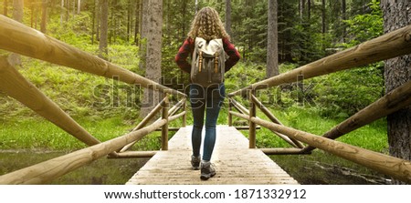 Hiking nature outdoor background - Young pretty girl woman with curly hair and backpack on her back hikes on a bridge in the forest (Black Forest Germany)