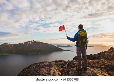 Hiking In Norway, Silhouette Of Hiker Looking At Beautiful Fjord Landscape And Holding Norwegian Flag, Adventure Outdoors