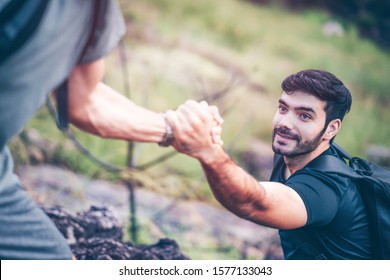 Hiking Outdoor Activity In Summer, Man Helping To Pull A Beard Guy Climb On Mountain. Climber Teamwork Trust And Support Each Other To Success. People Holding Hands To Rescue Team Together.  
