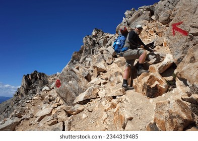 Hiking in Patagonia, Man with big backpack on steep loose rock mountainside Cerro Catedral mountain in Nahuel Huapi National Park, Red arrow trail mark way to Refugio Frey, Argentina - Powered by Shutterstock