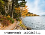 A hiking path curves along the edge of Jordan Pond through a forest in brilliant fall colors in Acadia National Park, Maine, USA