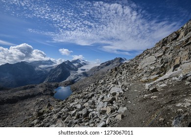 Hiking Path from Passo Presena to Passo Lagoscuro with Background of Mandron Glacier and Lake Lagoscuro and a cloudy blue sky