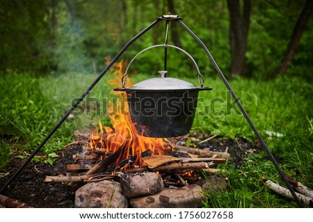 Hiking pot, Bowler in the bonfire. Fish soup boils in cauldron at the stake. Traveling, tourism, picnic cooking, cooking at the stake in a cauldron, fire and smoke.