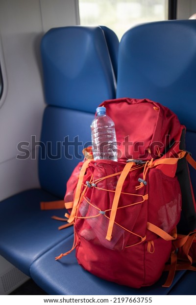 Hiking a red\
tourist backpack with a bottle of water in an electric train car.\
Concept: travel, weekend, vacation, rekking. adventure, art,\
travel. Camping holiday.  Tourist backpack\
