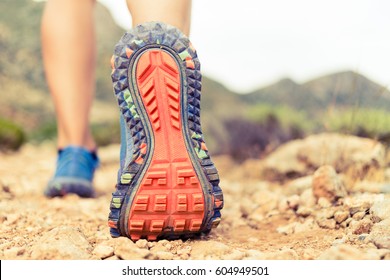 Hiking or running woman in beautiful mountains inspirational landscape. Sole of sports shoe and legs on rock trail. Hiker trekking or walking of footpath. Healthy fitness lifestyle outdoors.