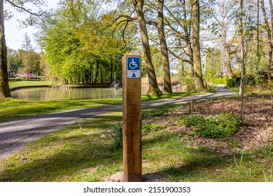 Hiking sign for disabled people in a park, drawing and the word Rolstoel means wheelchair, a path, pond and trees in the background, sunny day in Heidekamp Park, Stein, South Limburg, Netherlands - Shutterstock ID 2151900353
