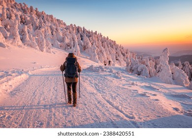 Hiking in snow at winter mountain during sunset. Woman with backpack and nordic walking poles trekking in cold weather. Sports and outdoors seasonal activity - Powered by Shutterstock