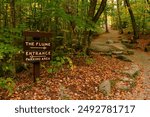 A hiking trail in the forest splits in two, with a sign leading hikers towards the flume or back to the entrance in Franconia Notch State Park in New Hampshire