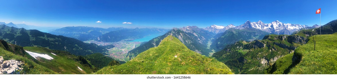 hiking trail panorama in the swiss mountains alps in summer / spring. Panoramic view at the summit of the mountain with the swiss national flag