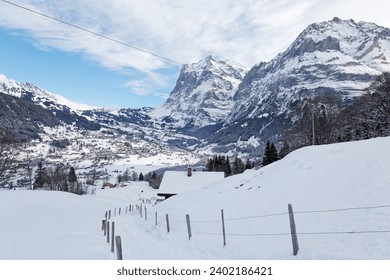 A hiking trail winding on the snowy hill towards Grindelwald village in the valley on a sunny winter day, with majestic Wetterhorn mountain towering in background, in Bernese Highlands, Switzerland - Powered by Shutterstock