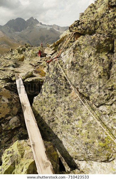 Hiking trail with\
wooden bridge, rope on stone and hiking trail sign, Valais,\
Switzerland, August\
2017.