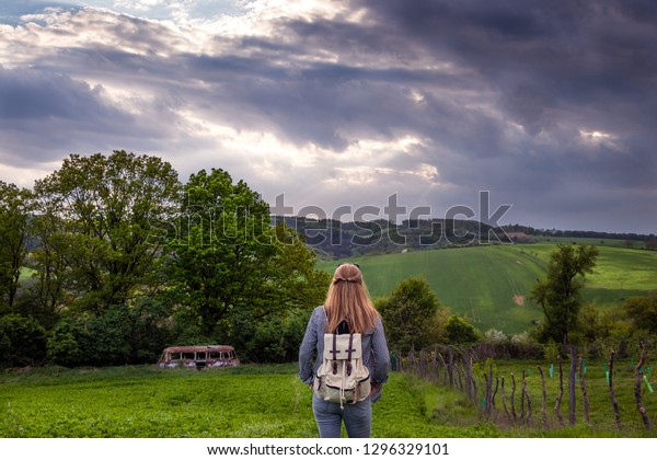 Hiking woman is enjoying\
view to spring landscape with dramatic sky. Young tourist walking\
in countryside