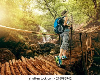 Hiking. Woman hikers walking on a bridge on the forest in the mountains on the waterfall. Girl with a backpack and sneakers traveling outdoors. Adventure in a hike. - Powered by Shutterstock