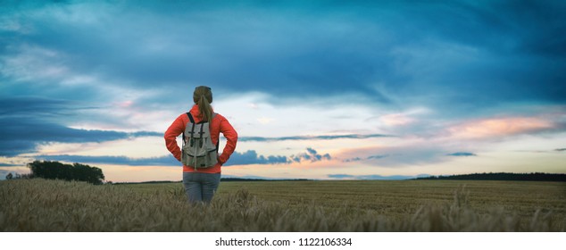 Hiking woman is standing in field and watching horizon with beautiful sky after sunset, panorama of countryside  - Powered by Shutterstock