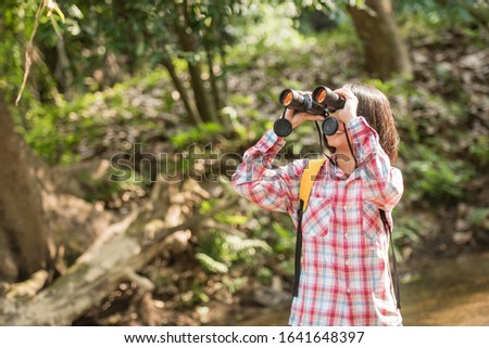 hiking women use binoculars to travel and have a happy smile. tourist looking through binoculars considers wild birds in the jungle. bird watching tours. with backpack. travel concept