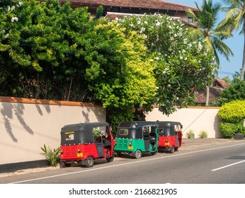 Hikkaduwa, Sri Lanka - March 4, 2022: Bright multi-colored tuk-tuks, Sri Lankan vehicles, stand outside the hotel under the trees along the road.