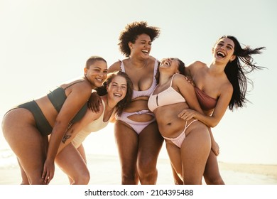 Hilarious female friends laughing cheerfully at the beach. Group of carefree friends having fun and enjoying their summer vacation. Happy young women together in swimwear.