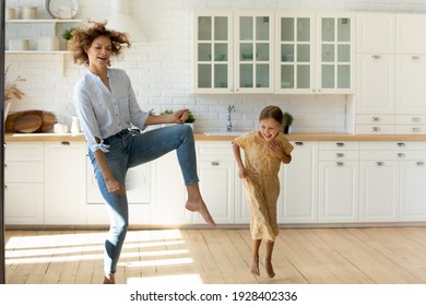 Hilarious Home Party. Emotional Family Young Single Mother And Small Daughter Having Fun Dance Listen To Music At New Modern Kitchen. Overjoyed Nanny Little Kid Girl Jump Barefoot On Warm Wooden Floor