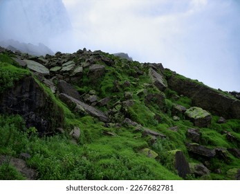 A hill with lush green, moss-covered rocks, water mist in the background.