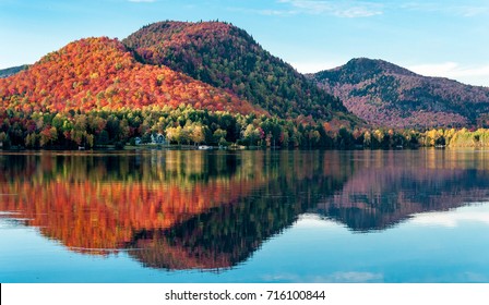 The hills covered with red maple forests are reflected in a lake in Quebec on a beautiful autumn evening