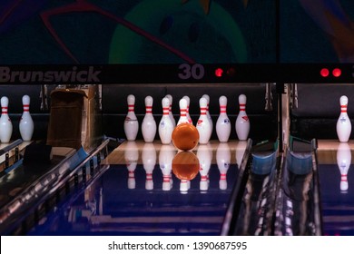 Hillsboro, Oregon \ USA - March 16 2019: Orange Bowling Ball Is About To Hit Center Of Pins At The End Of A Bowling Alley Reflecting On A Polished Lane Floor