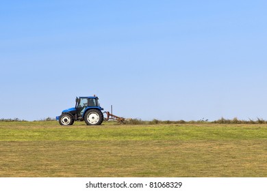 a hillside pasture with a blue tractor turning hay under a blue summer sky