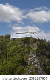A hillside with trees and architecture under a cloudy sky.
