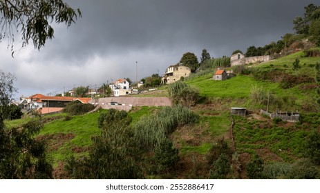 A hillside village with scattered houses and vibrant green fields under a dramatic, cloudy sky, showcasing the charm of rural life in a natural and scenic setting. - Powered by Shutterstock