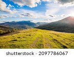 hilltop on the background of a mountain range with blue sky and sun rays on a teali summer day. Mountain landscape. 