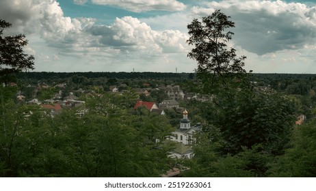 From the hilltop, a peaceful village stretches out beneath a sky filled with soft clouds. The trees frame the view, creating a calm and serene atmosphere. - Powered by Shutterstock