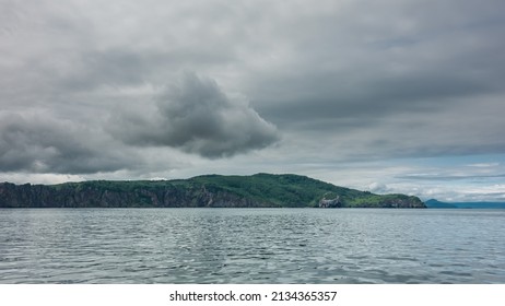 The hilly green coast of Kamchatka against a cloudy sky. Steep slopes of coastal cliffs. Ripples on the surface of the Pacific Ocean. Avacha Bay - Shutterstock ID 2134365357