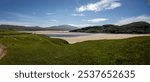 Hilly landscape with grass, daisies, dandelions, sand and sea water at low tide, on the coast of the North Atlantic Ocean near Cape Wrath and Sandwood Bay