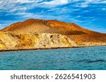 Hilly landscape on Mexican coast of Coronado Island, sparse vegetation, yellowish grass, blue sky with white clouds in background, Loreto Bay National Marine Park in Baja California Sur, Mexico