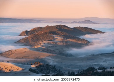 Hilly mountain range surrounded by fog during sunrise. Light from rising sun casts pink and orange hues. Dense forest covers parts of hills - Powered by Shutterstock