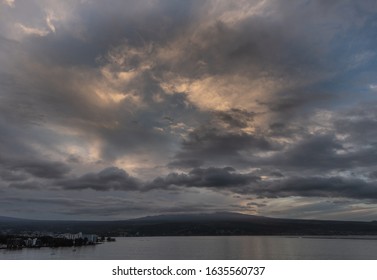 Hilo, Hawaii, USA. - January 14, 2020: Spectacular Dark Evening Cloudscape With Yellow Sunlight Patches Over Town And Volcano On Horizon.